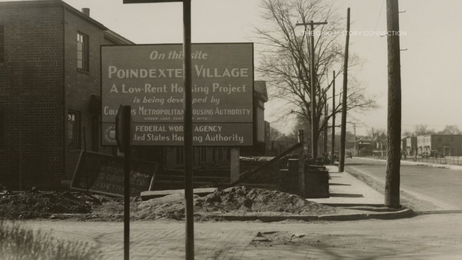 An old black-and-white photo of the original Poindexter Village shows the sign for the community on a street corner with the building behind it.