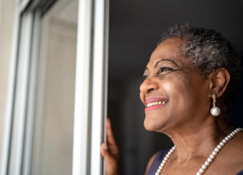 A middle-aged African American woman smiles as she looks out of her screen door.