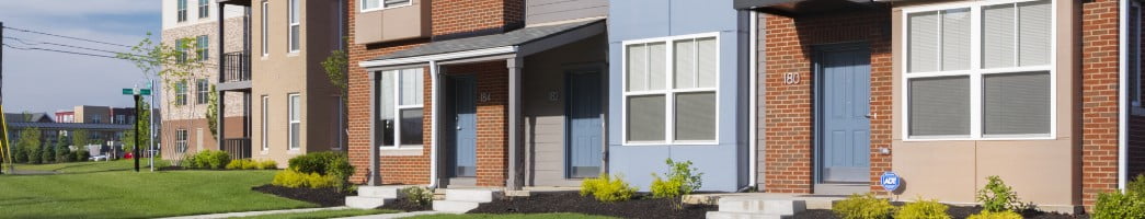A zoomed-in look of a townhouse shows a blue front door under a gray porch and front windows set into blue siding.