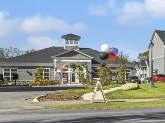 A large gray building sits off the road with nice landscaping and multicolor balloons tied in several spots with signs welcoming guests.