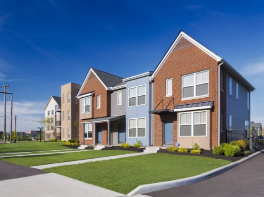  street view shows several townhouses lined up next to each other. Each is made up of brown brick, blue, tan and gray colors with a small lawn and nice landscaping out front.