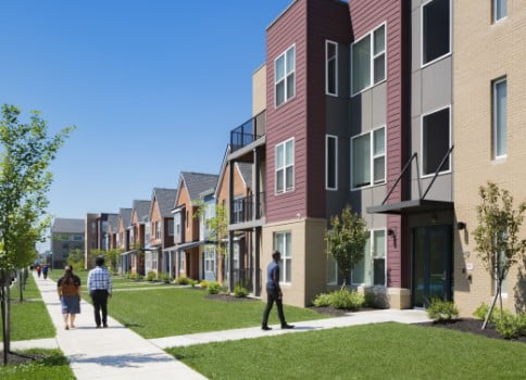 People walk down the street in front of an apartment complex and townhouses.