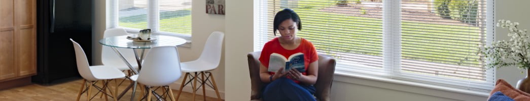 A young African American woman sits in her home reading a book.